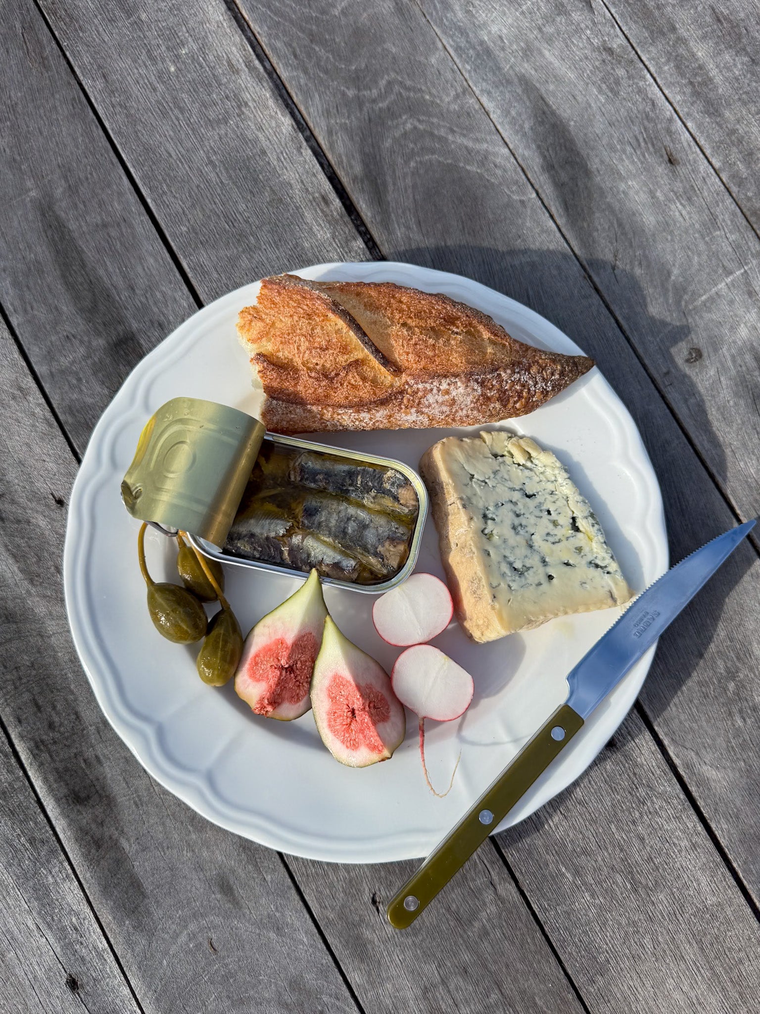 Plated meal with bread, sardines, figs, cheese and a knife on a wooden surface